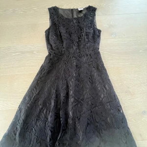 Svart spetsklänning från Vero Moda - Supersnygg svart klänning från Vero Moda i spets med blommigt mönster. Ärmlös modell med rund halsringning och lätt utställd kjol. Dragkedja bak för enkel påklädning. Perfekt för dig som vill ha en elegant look med lite edge.