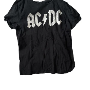 Svart AC/DC t-shirt - Svart t-shirt med stort AC/DC-tryck i vitt framtill. Klassisk rund hals och korta ärmar. Perfekt för dig som gillar rock och vill ha en avslappnad stil. Tillverkad i mjuk bomull för skön känsla hela dagen.