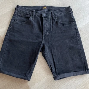 Svarta jeansshorts från Lee W32 - Snygga svarta jeansshorts från Lee med klassisk femficksdesign och uppvikta benslut. Shortsen har normal passform och stängs med knapp och dragkedja. Perfekta för en chill sommarstil.