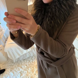 Rockandblue kappa med pälsdetalj - Snygg brun kappa från Rockandblue med stor fluffig fuskpäls runt kragen och knytskärp i midjan. Klassisk och stilren modell som ger en lyxig känsla. Perfekt för kyliga dagar när du vill vara både varm och trendig.🤎🌟🙏🥰