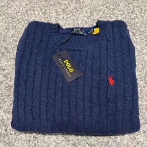 Blå stickad tröja Polo Ralph Lauren - Helt ny Kabelstickad blå tröja från Polo Ralph Lauren med klassisk rund hals och röd broderad logga på bröstet. Tröjan har Ettiketen kvar. PRISER KAN DISKUTERAS!!