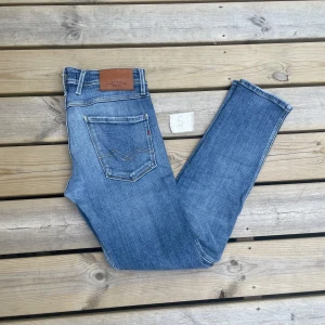 Replay Anbass ljusblå slim fit jeans 31-32 - Snygga ljusblå Replay Anbass jeans med klassisk femficksdesign och diskreta slitningar framtill. Jeansen har normal passform, raka ben och detaljer som Replay-logga på myntfickan och läderpatch bak i midjan. Perfekta för en avslappnad och trendig look.