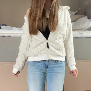 Vit teddyjacka från True North - Supermjuk och fluffig vit teddyjacka från True North med huva och dragkedja framtill. Jackan har ribbade muddar.. Snygg detalj med svart True North-logga på ärmen. 💞