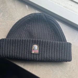 Svart ribbstickad mössa Parajumpers - Svart ribbstickad mössa från Parajumpers med uppvikt kant och broderad P.J.S-logga framtill. Klassisk och stilren modell som passar perfekt när det är kallt ute. Materialmix med ull och syntet för både värme och komfort.