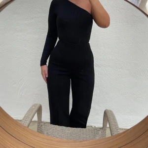 Svart oneshoulder topp - Säljer en superfin svart oneshoulder body som är ribbad och har en tight passform. Perfekt för en utekväll eller fest! Den är långärmad och ger en elegant look. Toppen är i nyskick och är liten i storleken.