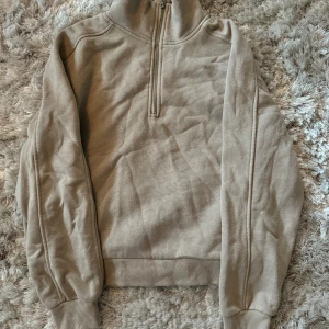 Beige tröja med dragkedja - Säljer en supermysig beige tröja med dragkedja i halsen. Perfekt för höst och vinter! Den har långa ärmar och är gjord i ett mjukt material som känns skönt mot huden. Passar perfekt till både jeans och kjol för en avslappnad look.