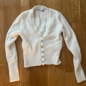 Stickad kofta - Vit stickad kofta från Zara. Köpt för tre år sedan men bara använd ett fåtal gånger, därav säljer jag. Koftan är v ringad och med silvriga knappar som ger en fin detalj. 