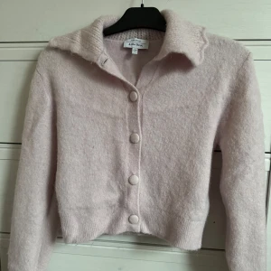 Ljusrosa/lila kofta från & Other Stories - Säljer en söt ljusrosa kofta från & Other Stories. Den har en mjuk och fluffig textur med knappar framtill och en ribbad krage. Perfekt för kyliga dagar och ger en mysig känsla. Passar bra till både jeans och kjol.
