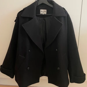 Svart oversized kappa från NA-KD - Snygg oversized svart kappa från NA-KD med klassisk design. Jackan har stora slag och knappar framtill samt fickor på sidorna. Perfekt för kyligare dagar med sin stilrena look.