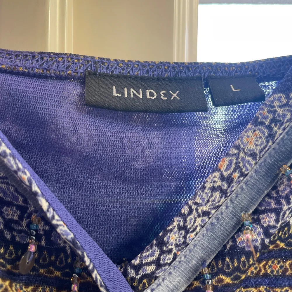 Säljer en jättefin ”vintage” blus från Lindex med ett unikt mönster. Påminner om 2000 - talet. Klänningen har en v-ringad design med dekorativa paljetter framtill. Perfekt för dig som vill sticka ut med stil i sommar!! Den va nämligen min mammas gammla som hon använde som klänning, därför är den i storlek L, så jag har sytt in den till strlk S/XS så den sitter bättre i passform. De går hur bra som helst att sprätta upp den, då jag ej har klippt av resterande tyg🤗 Hör av vid intresse!!❤️. Puserot.