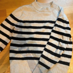 Randig tröja i beige och svart - Säljer en snygg randig stickad tröja i beige och svart. Tröjan har långa ärmar och en bekväm passform. Perfekt för en stilren look. Lite nopprig annars bra skick !