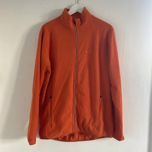 Orange fleecejacka från Everest - Säljer en orange fleecejacka från Everest med dragkedja framtill. Jackan har långa ärmar och två fickor med dragkedja. Perfekt för kyliga dagar och ger en skön och varm känsla.