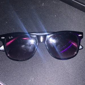 Svarta solglasögon från Ray-Ban - Klassiska svarta solglasögon från Ray-Ban med en stilren design. De har en robust båge och mörka linser som ger ett coolt och tidlöst utseende. Perfekta för soliga dagar och en stilren look.