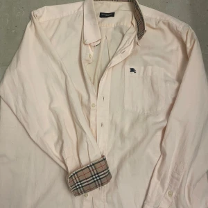 Burberry skjorta - Säljer en stilren skjorta från burberry med det ikoniska rutiga mönstret både i kragen och i ärmarna. Skjortan har samt burberrys hästlogga på bröstet. 