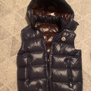 Moncler väst - Säljer en snygg svart dunväst från Moncler med glansig yta och dragkedja. Västen har en broderad Moncler-logga på bröstet och en quiltad design. Perfekt för kyligare dagar. Priset kan diskuteras ungefär helt ny 