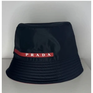 Svart bucket hat från Prada -  svart bucket hat från Prada med röd logotypdetalj. Helt ny, priset går att diskutera 