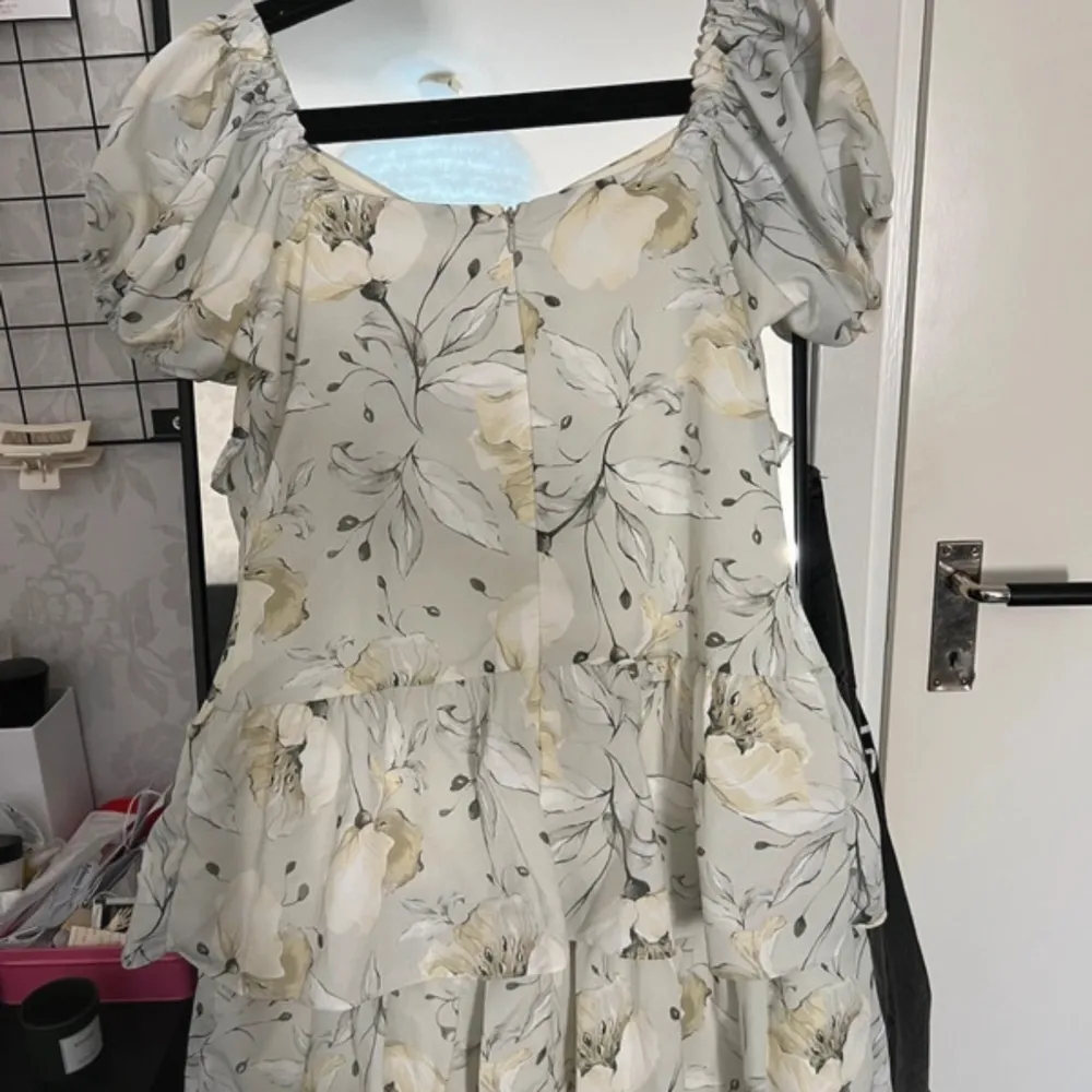 Charmig blommig klänning från Trendyol med volanger och korta ärmar. Klänningen har en ljus bas med stora blommönster i dämpade toner. Perfekt för en somrig look med sin luftiga design och romantiska stil.. Mekot.