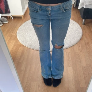 Blå bootcut jeans med slitningar - Säljer ett par lågmidjade blå bootcut jeans med slitningar på knäna. 