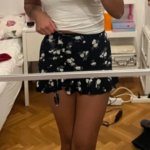Blommig kortkjol från Hollister - Snygg blommig kortkjol från Hollister i mörkblått med vita blommor. Kjolen har shorts undertill och en dradkedja på ena sidan. Perfekt för en somrig look!