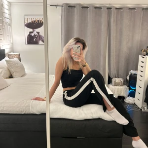 Svarta byxor med vita ränder - Snygga svarta byxor med vita ränder längs sidorna. Byxorna har en loose passform och är perfekta för en avslappnad stil. De är högmidjade och har en sportig look.