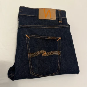 Mörkblå jeans från Nudie Jeans - Snygga mörkblå jeans från Nudie Jeans med klassisk femficksdesign och kontrasterande orange sömmar. Lean Dean 33/32