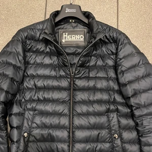 Herno jacka  - Snygg svart pufferjacka från Herno med dragkedja och ribbade muddar. Jackan har en stilren design med två fickor framtill och är perfekt för kyligare dagar. Den är lätt och bekväm att bära.