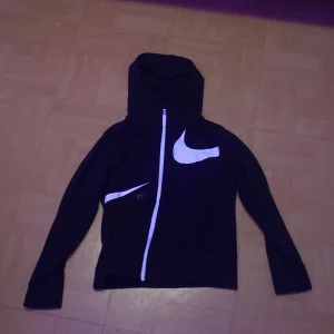 Svart hoodie från Nike - Tjenare! Säljer en svart fleece från Nike med stor vit logga på bröstet och ärmen. Fleecen har dragkedja och huva, perfekt för en sportig look. Passar för längd 147-158 cm. Använd max 1 gång, bra skick! Tveka inte på att höra av dig om du undrar nåt 