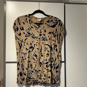 Beige leopardmönstrad topp - Snygg beige topp med leopardmönster i svart och vitt. Toppen har en rund halsringning och korta ärmar. 