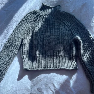 Grön  stickad polotröja - Säljer en snygg grön stickad polotröja med croppad passform. Tröjan har långa ärmar och en hög krage som ger en stilren look. 