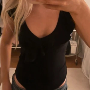 Svart volangbody - Snygg body med djup v-ringning. Passar bra till jeans eller kjol.