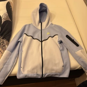 Ljusblå hoodie från Nike - Säljer en ljusblå hoodie från Nike med dragkedja och huva. Den har svarta detaljer och en ficka på ärmen. Perfekt för en sportig look eller avslappnad stil. 🌀