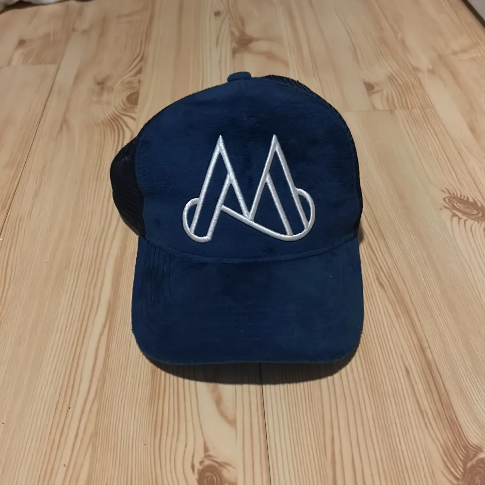 Snygg blå keps med vit broderad logga framtill. Kepsen har ett nätmaterial baktill för bättre ventilation och justerbar passform. Perfekt för en avslappnad stil. Ny pris är 549. Asusteet.