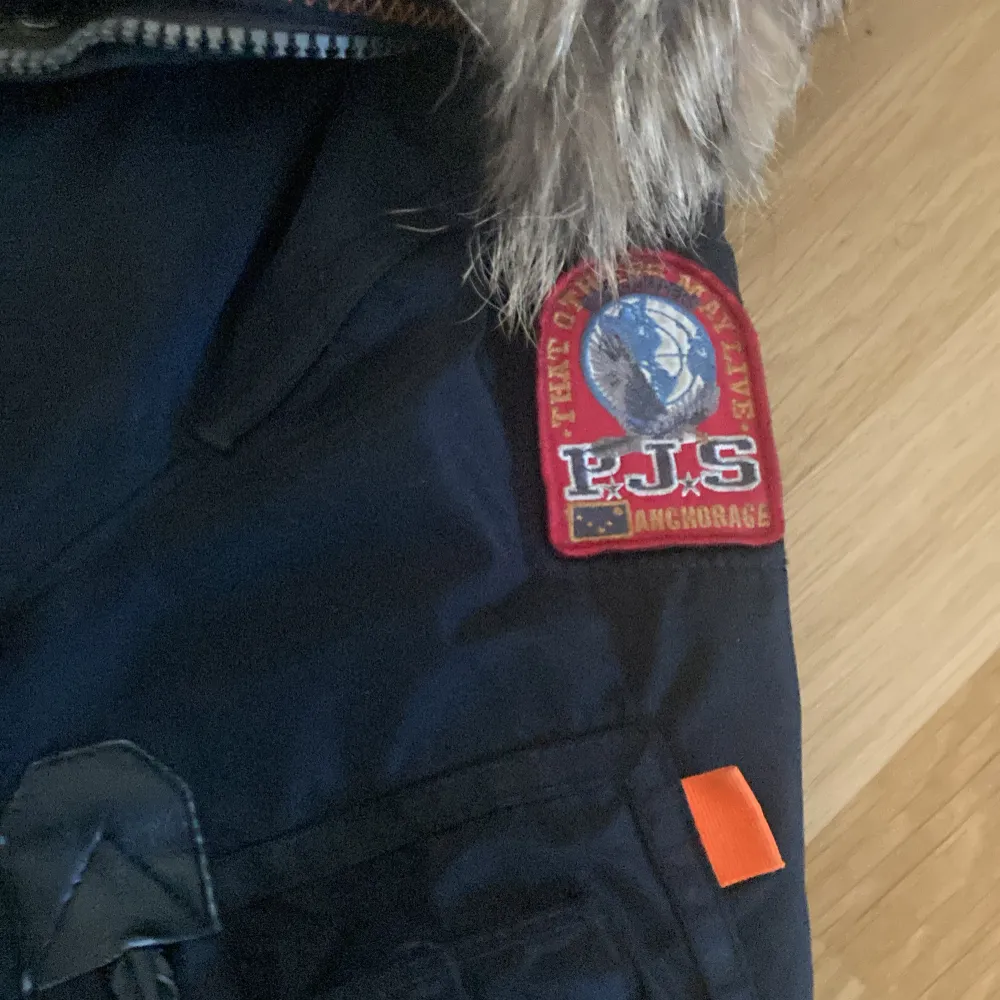 Säljer en svart Parajumpers vinterjacka i storlek small. Jackan har en avtagbar pälsfodrad huva och flera praktiska fickor. Den är perfekt för kalla vinterdagar och har snygga detaljer som en gul rem och en PJS-logga på ärmen. Dragkedja och knappar framtill för extra värme.🖤obs ‼️ endast frakt. Frakt PostNord . Jackor.