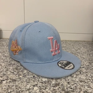 LA keps säljes - LA keps säljes i använd nyskick. Färgen är ljusblå och LA märket är rosa. Kan hämtas i Skärholmen. Vid intresse är det bara att höra av sig.