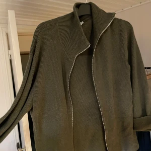 Olivgrön stickad tröja från Ljung - Säljer en olivgrön stickad tröja från Ljung by Marcus Larsson. Den har en dragkedja framtill och en hög krage som ger en stilren look. Perfekt för kyliga dagar och passar både till vardags och lite finare tillfällen. Tröjan är i storlek XL och är superbekväm att ha på sig.