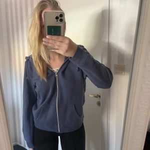 Mörkblå hoodie med dragkedja - Säljer en mörkblå hoodie med dragkedja framtill. Den har en klassisk design med långa ärmar och en justerbar huva med snören. Perfekt för en avslappnad stil och passar bra till både höst och vår. Den har också praktiska fickor framtill. 