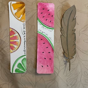 Bokmärken - Säljer tre unika bokmärken: ett med citrusmotiv och texten 'Each day is a chance to grow', ett med vattenmelonmotiv och arabisk text, samt ett i form av en brun fjäder. Perfekta för att hålla koll på läsningen med stil! 🍉🍊🪶