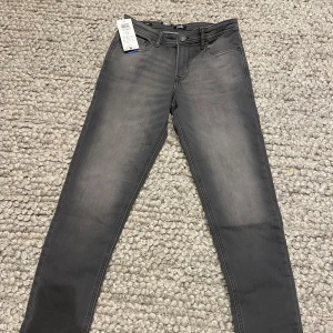 Grå slim jeans från Jack & Jones strl 164 - Snygga grå slim fit jeans från Jack & Jones, modell Glenn. Perfekta för en stilren look med klassisk femficksdesign och knappgylf. Passar utmärkt för en ungdomlig stil. Helt nya med taggar kvar. 