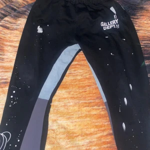 Svarta byxor från Gallery Dept. - Coola svarta byxor från Gallery Dept. med unika vita färgstänk och tryckdetaljer. Byxorna har en avslappnad passform och elastisk midja för extra komfort. Perfekta för en trendig och avslappnad stil.