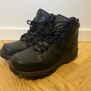 Svarta Nike Manoa boots stl 41 - Snygga svarta boots från Nike i skinn med robust snörning och en kraftig sula. Perfekta för höst- och vinterväder. Diskret Nike-logga på sidan ger en stilren look.