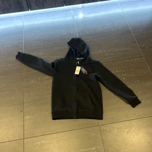 Svart hoodie från Ralph Lauren - Säljer en stilren svart hoodie från Ralph Lauren. Den har en dragkedja framtill och en klassisk huva. Perfekt för en avslappnad look.