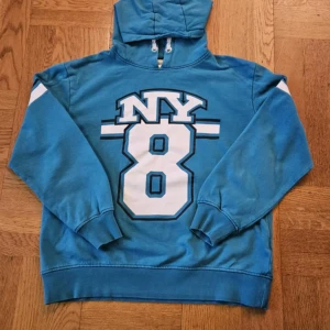 Blå hoodie från bpc - Säljer en blå hoodie från bpc med trycket 'NY 8' på framsidan. Tröjan har långa ärmar och en praktisk huva med snörning. Perfekt för en avslappnad stil. 