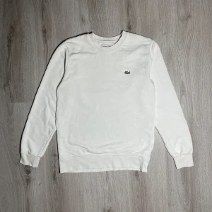 Vit sweatshirt från Lacoste - Säljer denna tröja för att den är för liten på mig, ser nästan oanvänd ut, har bara använt den ett par gånger men inte ofta för att jag har enkelt för mig att smutsa ner vita kläder så jag hade inte på mig den så ofta, storlek S men passar M