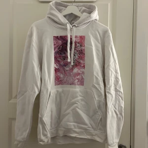 Vit hoodie från The cool Elephant - Säljer en vit hoodie från The cool Elephant med en unik rosa och svart illustration på framsidan. Hoodien har en klassisk känguruficka och justerbar dragsko i huvan. Perfekt för en avslappnad stil.