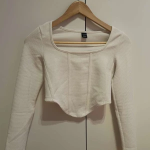 Vit ribbad topp  - Säljer en stilren vit ribbad topp. Den har en fyrkantig urringning och långa ärmar. Toppen är croppad och passar perfekt för en trendig look.