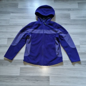 Lila fleecejacka från On The Peak - Säljer en lila fleecejacka från On The Peak med huva och dragkedja. Jackan har svarta snören vid huvan och kontrasterande ljuslila paneler på ärmarna. 