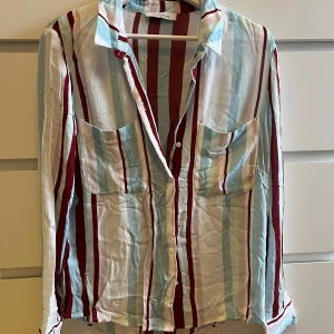 Randig skjorta med fickor från Samsøe & Samsøe - Snygg randig skjorta i ljusblått, vinrött och vitt. Skjortan har långa ärmar och två bröstfickor. 