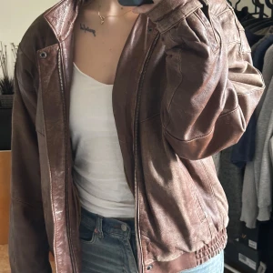 Brun skinnjacka - Säljer en snygg brun skinnjacka med dragkedja och långa ärmar. Jackan har en cool, avslappnad stil med en loose passform. Perfekt för att ge din outfit en edgy touch.