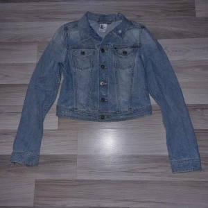 Ljusblå jeansjacka från H&M - Säljer en klassisk ljusblå jeansjacka från H&M. Jackan har en normal passform med långa ärmar och knappar framtill. Knappt använd men har "slitna" detaljer. Perfekt för vår och sommar! 🌼 
