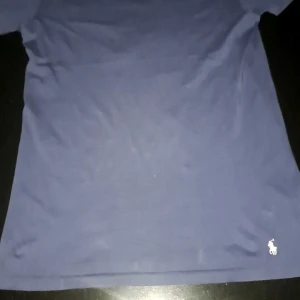 Blå t-shirt från Ralph Lauren - Säljer en riktigt blå t-shirt från Ralph Lauren med det ikoniska broderade logotypen i vitt. Perfekt för en stilren och avslappnad look. T-shirten är kortärmad och tillverkad i mjukt bomullsmaterial. Storlek M men passar även S, hör av er!